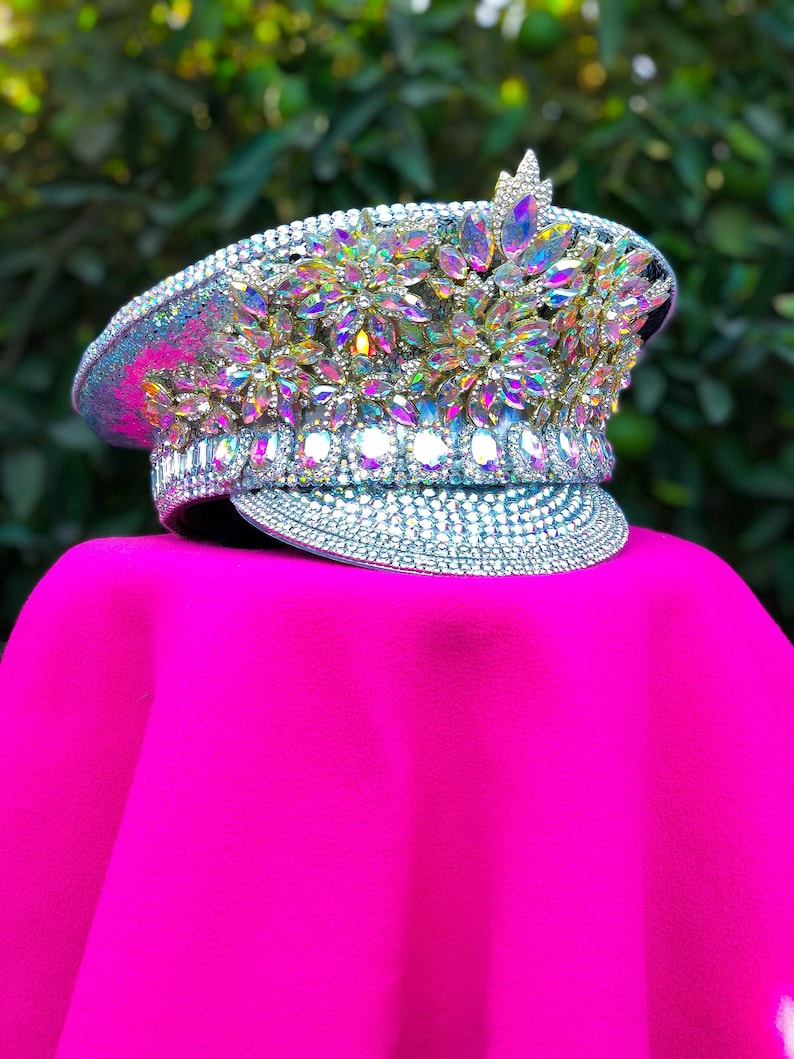 May include: A silver and white hat with iridescent rhinestones and a pointed crown. The hat is sitting on a bright pink surface.