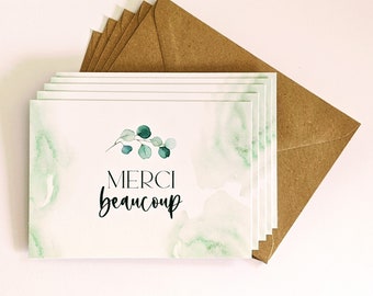 Può includere: Un set di biglietti di ringraziamento con uno sfondo ad acquerello e un design di ramo di eucalipto verde. I biglietti dicono "Merci beaucoup" in lettere nere.