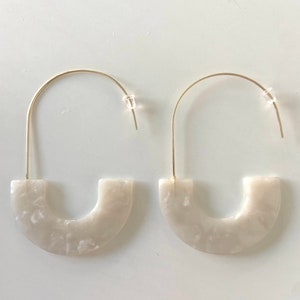 May include: A pair of white, marbled, hoop earrings with a gold wire and a gold hook closure.