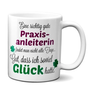 May include: White ceramic mug with a black and purple inscription that reads "Eine richtig gute Praxis-anleiterin findet man nicht alle Tage... Gut, dass ich soviel Glück hatte."  The inscription is surrounded by green four-leaf clover graphics.