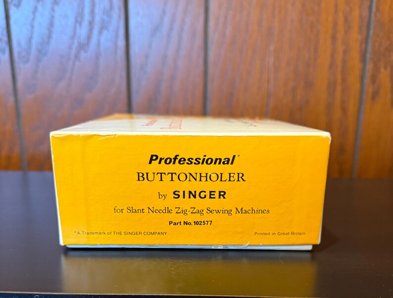 May include: A yellow box with the text "Professional Buttonholer by SINGER for Slant Needle Zig-Zag Sewing Machines Part No. 102577" and "A Trademark of THE SINGER COMPANY Printed in Great Britain".