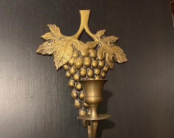 May include: A gold-toned brass wall sconce with a grapevine design and a candle holder.