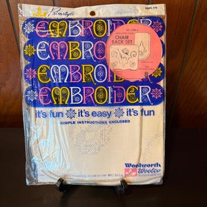 May include: A package of white embroidery fabric with blue and pink scalloped edges. The package includes instructions for a chair back set. The package is labeled "Primstyle" and "Woolworth Woolco".