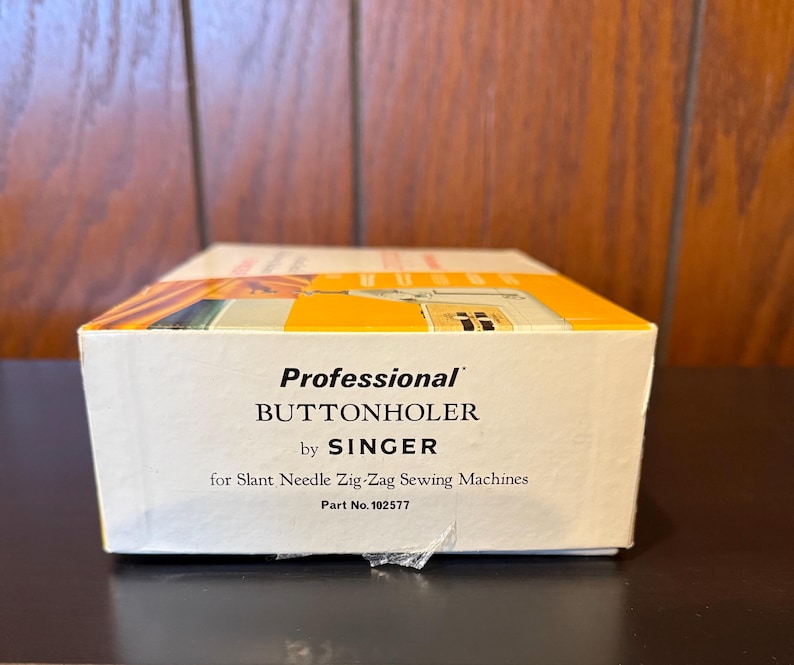 May include: A white box with the text "Professional Buttonholer by SINGER for Slant Needle Zig-Zag Sewing Machines Part No. 102577"