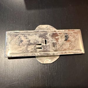 May include: A silver-toned metal plate with a keyhole and two small slots. The plate has a slightly worn, aged appearance.