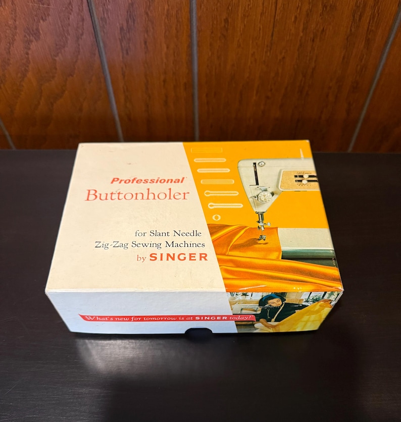 May include: A white box with a yellow and orange design. The box is labeled "Professional Buttonholer for Slant Needle Zig-Zag Sewing Machines by SINGER". The box features a vintage Singer sewing machine and a woman sewing.