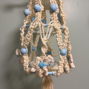 May include: A white macrame hanging mobile with blue beads and ceramic horses. The mobile has a tassel at the bottom.