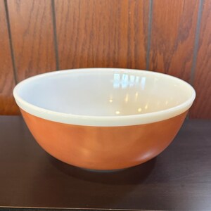 May include: A round mixing bowl with a smooth, opaque white interior and a solid, vibrant orange exterior. The bowl features a wide, circular rim and a deep, curved basin, constructed from a glossy, milk glass material with a consistent finish.