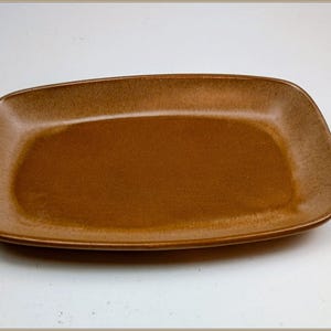 以下が含まれることがあります： 丸みを帯びた角を持つ長方形の茶色のセラミック製サービングプラッター。プラッターは滑らかで光沢のある表面を持ち、食品の提供用に設計されています。色は暖かくアースカラーです。
