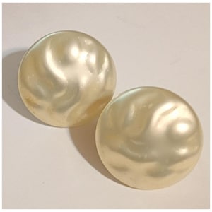 May include: Two large, round, cream-colored earrings with a pearlescent finish. The earrings have a slightly swirled pattern on their surface, and are set against a white background. These earrings are a classic accessory.
