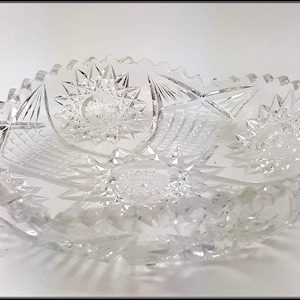 Puede incluir: Cuenco de cristal tallado transparente con diseño de estrella y geométrico. El cuenco tiene un borde festoneado y probablemente es de cristal. El cuenco es de forma ovalada y se encuentra sobre una superficie blanca.