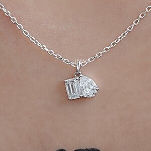 May include: A delicate silver necklace featuring a pendant with two diamond-cut gemstones. One is an emerald cut, and the other is a pear shape. The necklace is displayed against a neutral background.