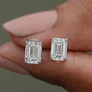 May include: A pair of emerald cut diamond stud earrings. The earrings are set in a silver metal setting.