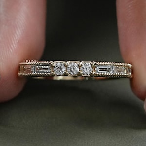 以下が含まれることがあります： 小さな丸いダイヤモンドとバゲットダイヤモンドが並んだ、繊細なゴールドのバンドリングです。