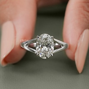 Puede incluir: Un anillo de tono plateado con una piedra preciosa transparente de corte ovalado en el centro, sujeta por cuatro garras. La banda tiene un diseño de vástago dividido que se estrecha hacia la piedra central. La palabra EBUNG está impresa.