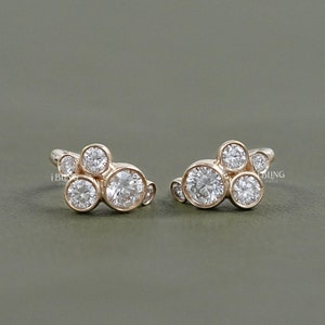 以下が含まれることがあります： 小さな丸い透明な石のクラスターが付いた、ゴールドのイヤリングのペア。イヤリングは雲の形をしています。