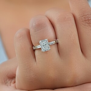 May include: A radiant-cut diamond engagement ring with a gold band. The ring features a large rectangular center stone and smaller baguette diamonds on the sides. The ring is on a person's finger.