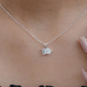 May include: A delicate silver necklace featuring a pendant with two gemstones: an emerald-cut and a pear-shaped diamond. The necklace is worn around the neck, showcasing the sparkling pendant.