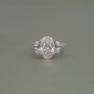 以下が含まれることがあります： オーバルカットのダイヤモンド婚約指輪。中央にオーバルカットのダイヤモンド、両側にペアシェイプのダイヤモンドがセットされています。シルバーのバンドにセットされ、輝きを放ちます。クラシックでエレガントなジュエリーです。