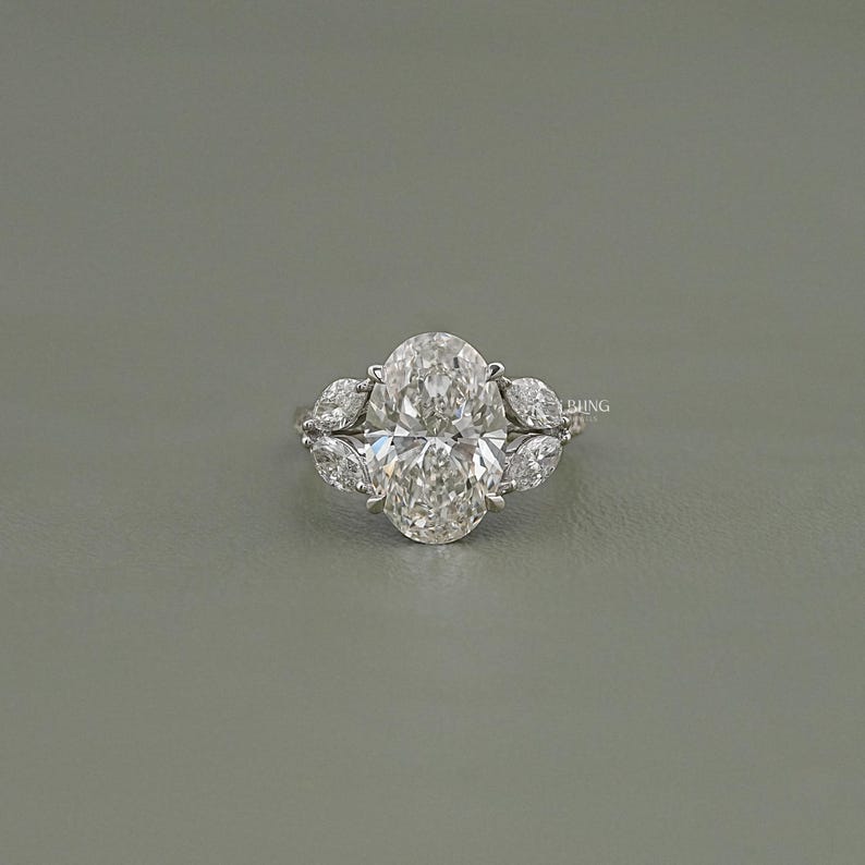 以下が含まれることがあります： オーバルカットのダイヤモンド婚約指輪。中央にオーバルカットのダイヤモンド、両側にペアシェイプのダイヤモンドがセットされています。シルバーのバンドにセットされ、輝きを放ちます。クラシックでエレガントなジュエリーです。