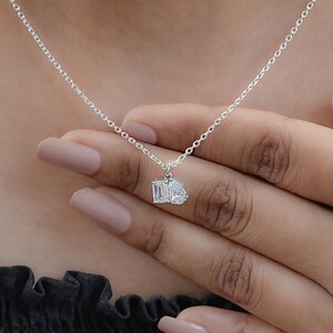 May include: A delicate silver necklace featuring a pendant with two white gemstones. One gemstone is an emerald cut, and the other is a pear shape. The necklace is displayed on a person's hand.