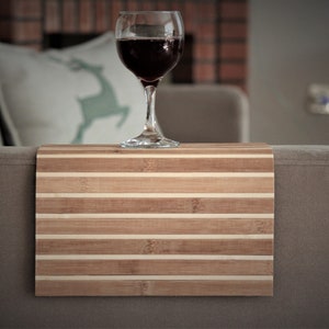 May include: A wooden tray with a striped pattern sits on a grey sofa. A glass of red wine sits on the tray.