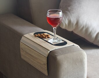 Könnte beinhalten: Ein Tablett aus Holz mit schwarzem Rand liegt auf einem beigen Sofa. Auf dem Tablett stehen ein Glas Rotwein und ein kleiner Haufen Mandeln.