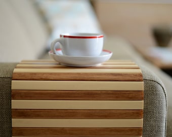 Può includere: Una tazza da caffè in ceramica bianca con una fascia rossa attorno alla parte superiore, appoggiata su un piattino bianco su un vassoio di legno con strisce di legno chiaro e scuro alternate.