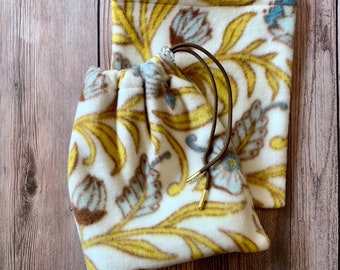May include: A white drawstring bag with a floral pattern in yellow, brown, and blue. The bag has a brown drawstring and a gold metal toggle.