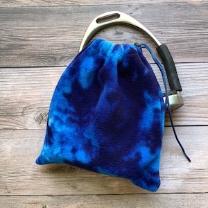 May include: A blue and navy tie-dye fleece stirrup leather bag with a drawstring closure. The bag is designed to hold a stirrup iron.