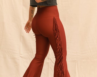 May include: A pair of rust-colored flared pants with fringe detail along the outside seams. The pants are made of a soft, stretchy fabric and have a high waist.