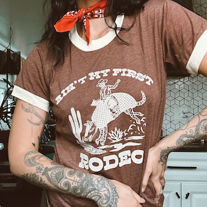 「Ain't My First Rodeo」レトロリンガーTシャツ、ディラス、ウエスタン、サウスウェストTシャツ、アルマジロシャツ、面白いグラフィックTシャツ、ハイキングシャツ