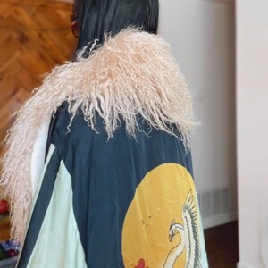 May include: A black and green kimono with a white crane and floral design. The kimono has a pink fluffy collar.