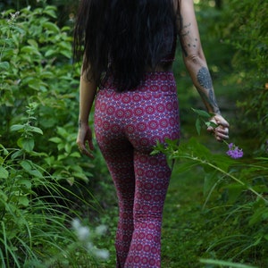 May include: A person wearing a pair of red and white patterned bell bottom pants in a forest setting.