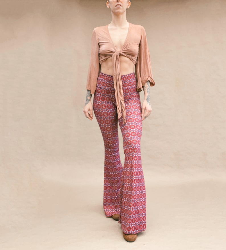 May include: A woman wearing a light brown crop top with a tie at the front and a pair of red, blue, and white patterned bell bottom pants.