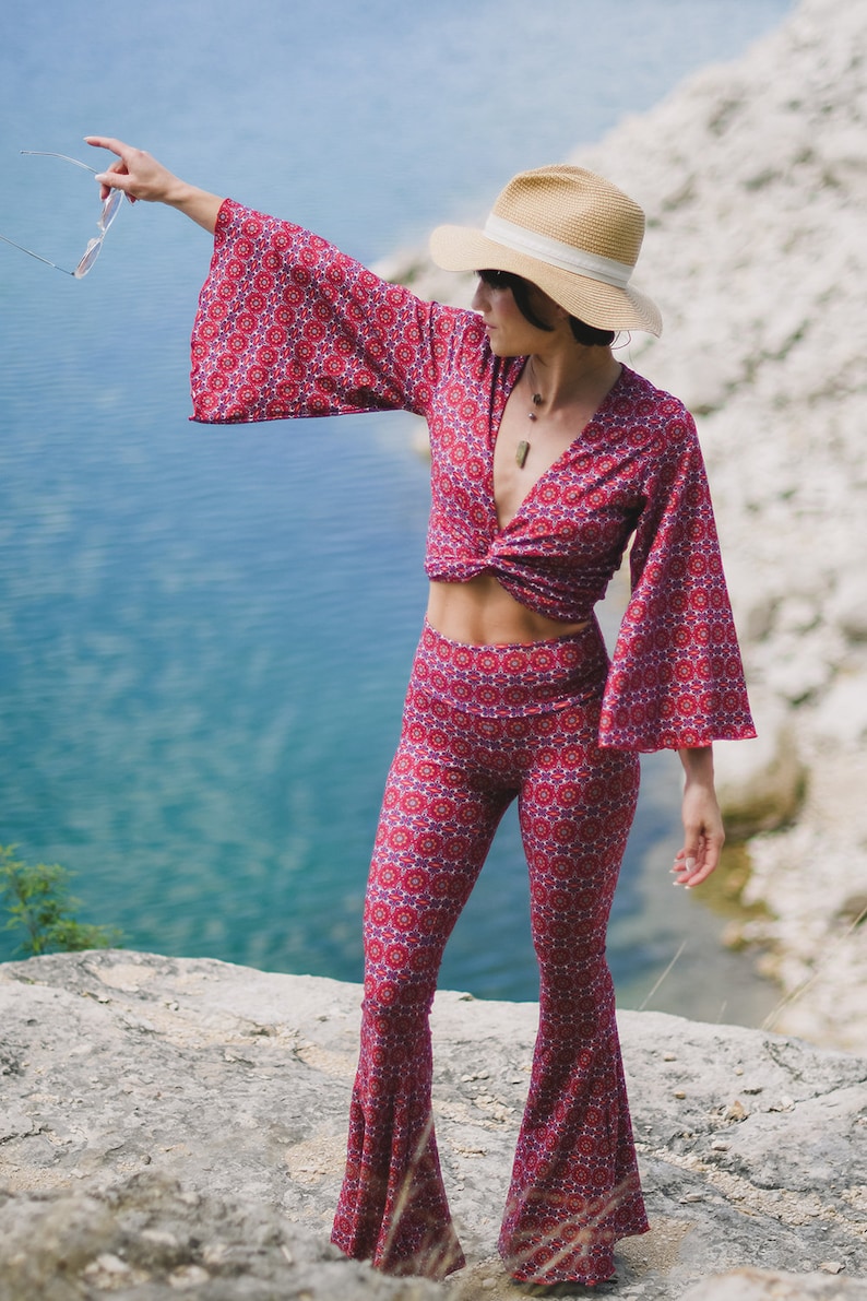 May include: A woman wearing a red and white patterned pantsuit with a wide-leg, bell-bottom style. She is wearing a straw hat with a white band and has a necklace on.