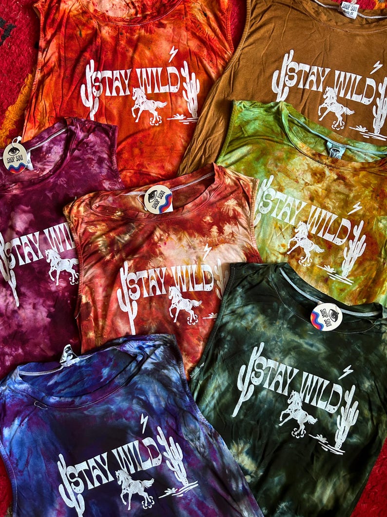 May include: A collection of six tie-dye tank tops with the phrase "Stay Wild" printed in white on each. The tank tops are in various colors, including orange, red, purple, green, and blue.