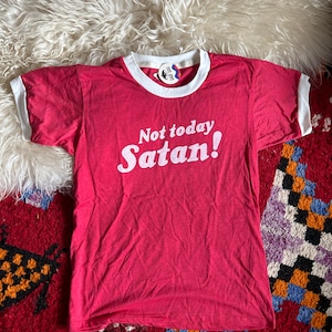 K&ouml;nnte beinhalten: Rotes T-Shirt mit wei&szlig;en Rippen an Kragen und &Auml;rmeln und wei&szlig;em Text "Not today Satan!"