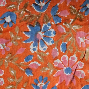 Peut inclure: Gros plan sur un tissu à motifs floraux. Le motif présente des fleurs bleues, roses et blanches avec des tiges et des feuilles marron sur un fond orange. Le tissu a un aspect texturé.