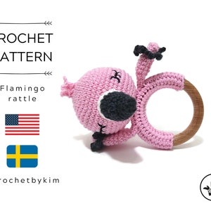 May include: Pink crocheted flamingo rattle with a wooden ring. The flamingo has black eyes and a black beak. The rattle is made for babies.