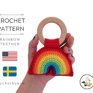 May include: A crocheted rainbow teether with a wooden ring. The teether is red, orange, yellow, green, blue, indigo, and violet. The teether is attached to the wooden ring with a red crocheted strap.