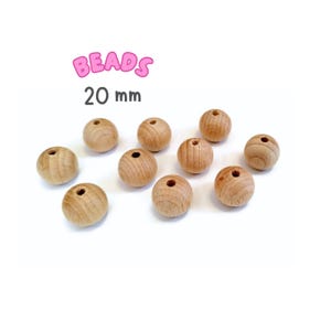 May include: Ten natural wood beads, each measuring 20 mm in diameter. The beads are round and have a hole in the center. The beads are arranged in a scattered pattern on a white surface. BEADS 20 mm is written in pink letters above the beads.