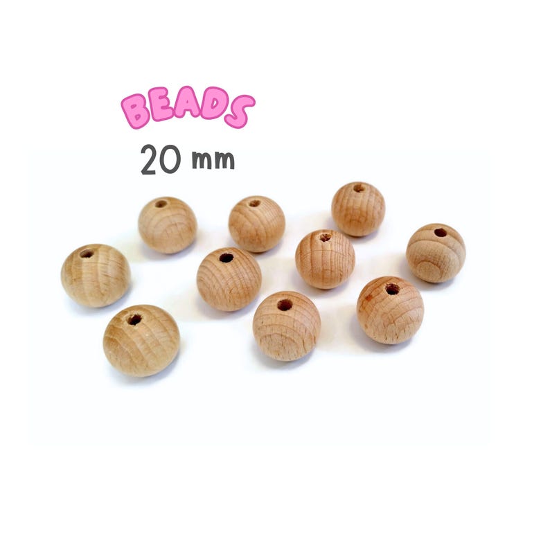 May include: Ten natural wood beads, each measuring 20 mm in diameter. The beads are round and have a hole in the center. The beads are arranged in a scattered pattern on a white surface. BEADS 20 mm is written in pink letters above the beads.