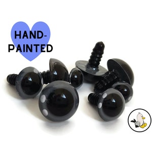 Pode incluir: Seis olhos de segurança de plástico preto com pupilas brancas e parafusos nas costas. Os olhos são pintados à mão e têm um acabamento brilhante.  HAND-PAINTED está escrito em azul sobre um fundo em forma de coração.