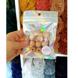 May include: A clear plastic bag filled with 10 natural wood beads, each measuring 20 mm in diameter. The bag has a pink label with the text "20 mm" on it.