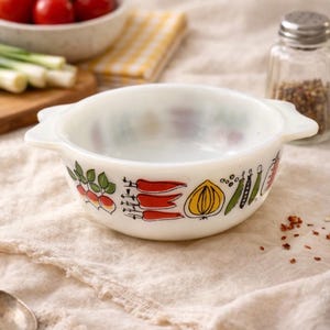 May include: A vintage white milk glass bowl with a colorful vegetable design. The bowl features illustrations of radishes, carrots, onions, and other vegetables. It has two handles and is perfect for serving side dishes or small portions.