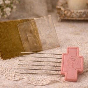 May include: A vintage hair styling tool with a pink handle and metal tines, alongside a gold-toned wallet and a clear plastic insert. The items are arranged on a lace surface, suggesting a focus on antique or retro hair accessories.