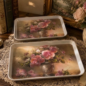 May include: Two rectangular white serving trays featuring a printed illustration of a bouquet of pink and white roses in a decorative vase. The trays have raised edges and a smooth finish, displaying a floral still life design on the surface.