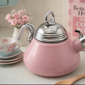 May include: A pastel pink tea kettle with a polished silver lid and handle. The kettle is on a kitchen counter. A teacup and saucer set with a floral design are in the background, alongside a vase of pink flowers.