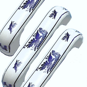 May include: Three white cabinet handles featuring a repeating dark blue bird and foliage pattern. Each handle has a curved, elongated shape with thin dark blue lines bordering the edges, showcasing a consistent decorative motif across all pieces.